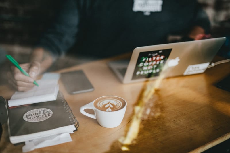 A laptop, notebook and latte on a cafe table